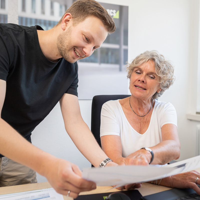 Zwei Personen an Schreibtisch im Gespräch über Blatt Papier