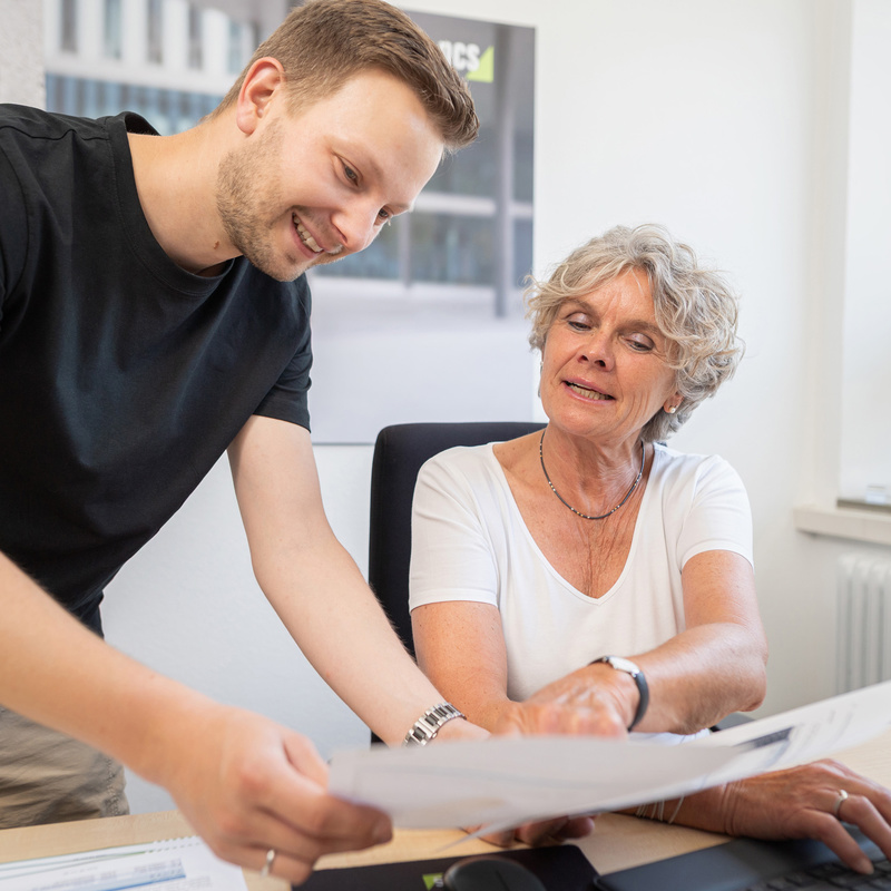 Zwei Personen an Schreibtisch im Gespräch über Blatt Papier