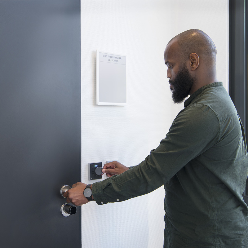 Person hält RFID-Tag an INTUS 700 neben schwarzer Türe