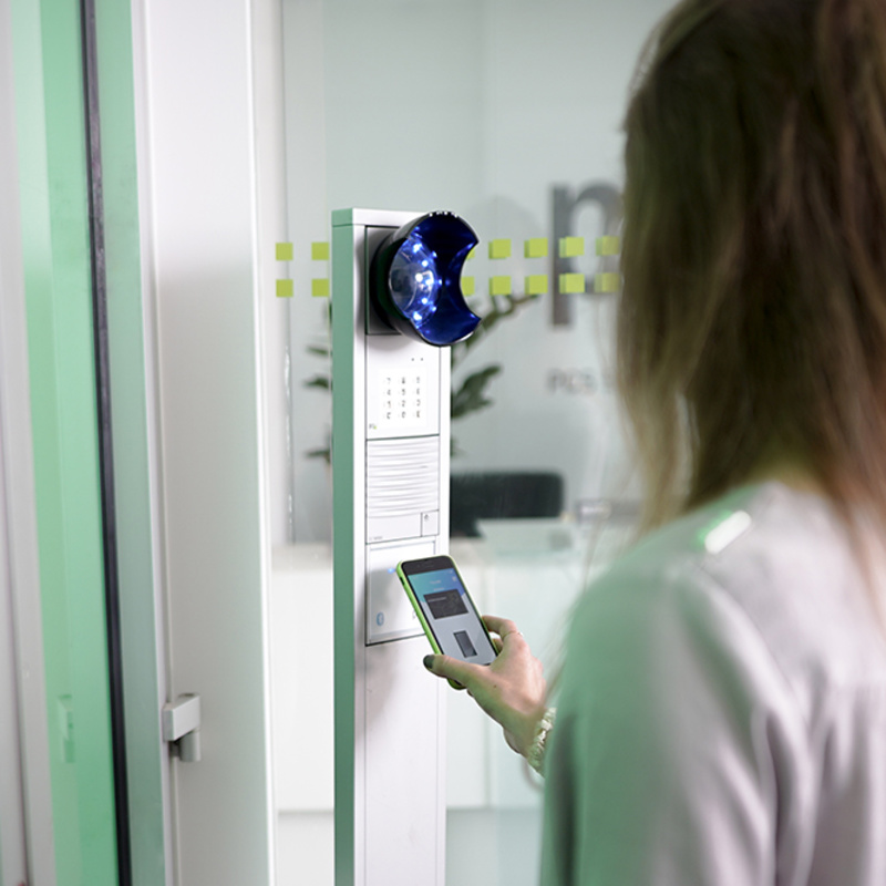 Frau mit Smartphone bedient INTUS 400 in Türkommunikationsanlage bei PCS
